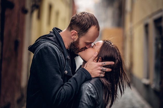 Hombre barbudo positivo besando a una linda morena en una calle de un casco antiguo.