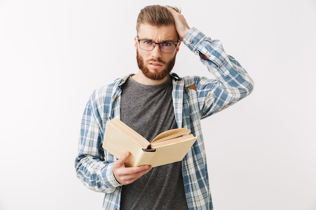 Hombre barbudo preocupado confundido en camisa y anteojos con libro