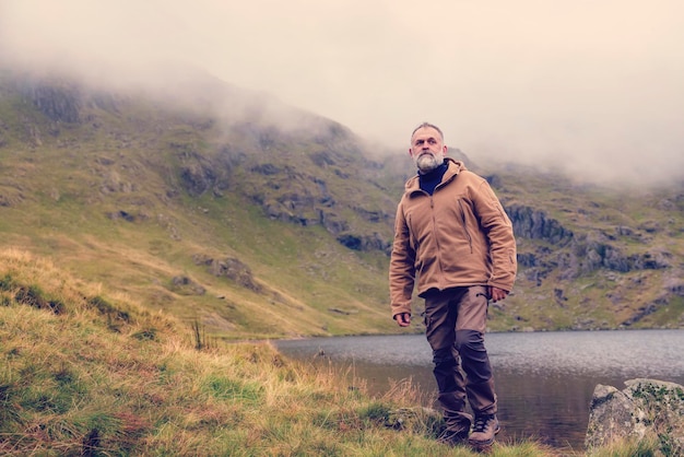 Hombre barbudo que llega solo al destino al lago en las montañas en un día brumoso de otoño