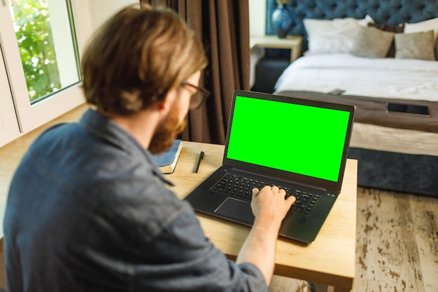 Hombre barbudo que usa el lugar de trabajo de la computadora portátil en casa con pantalla verde