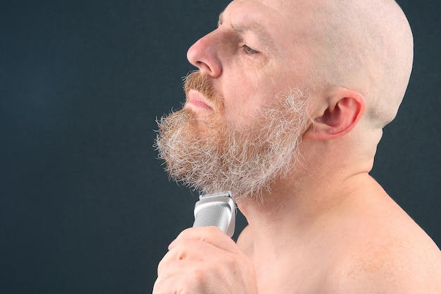 Hombre barbudo con recortador para ajustar la barba en la mano