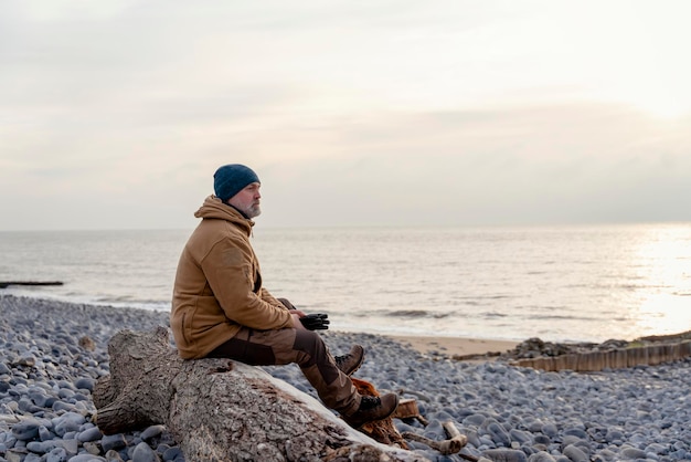 Hombre barbudo relajándose solo en la playa en el frío día de invierno Concepto de estilo de vida de viaje