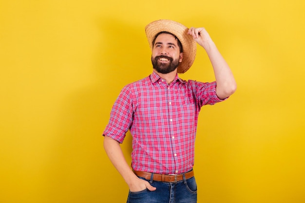 Hombre barbudo con ropa típica de fiesta Junina con la mano en el sombrero optimista Por la Fiesta de Arraia