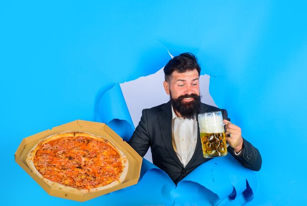 Hombre barbudo con sabrosa pizza y cerveza mirando a través del agujero de papel hombre satisfecho con barba y