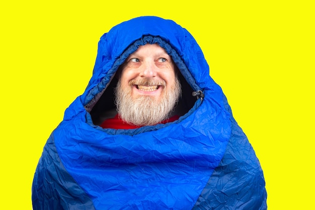 Foto hombre barbudo en un saco de dormir en un fondo amarillo equipos para la recreación en el turismo y los viajes