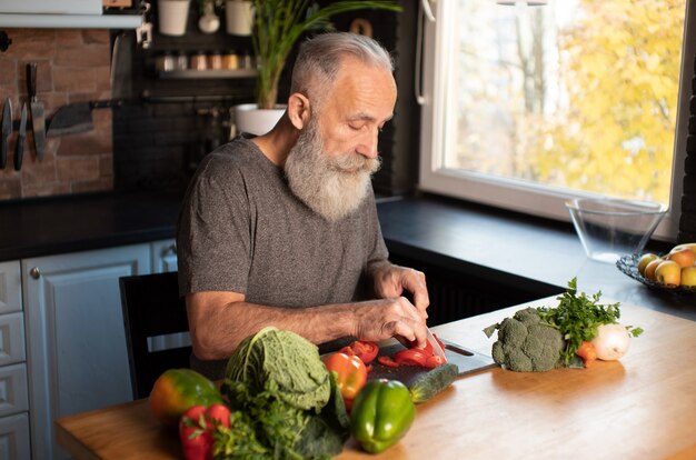 Hombre barbudo senior cortar verduras en el tablero de madera