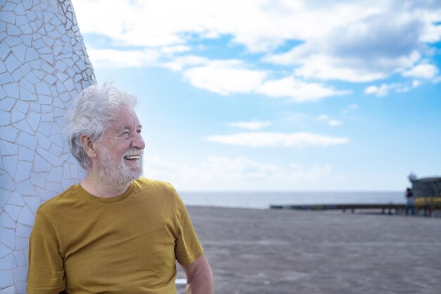 Hombre barbudo senior despreocupado riendo al aire libre en el mar, cielo nublado, horizonte sobre el agua