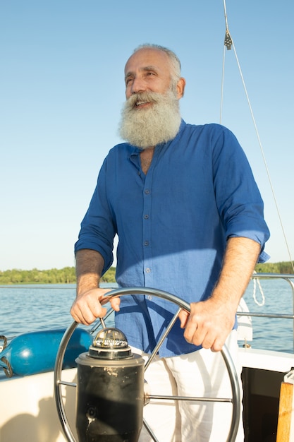 Hombre barbudo senior en velero o yate flotando en el lago.