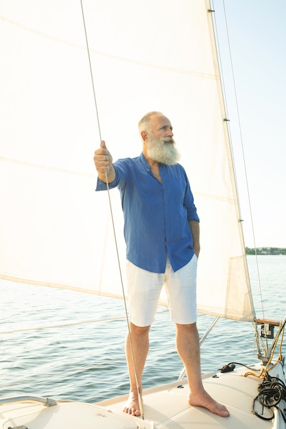 Hombre barbudo senior en velero o yate flotando en el lago.