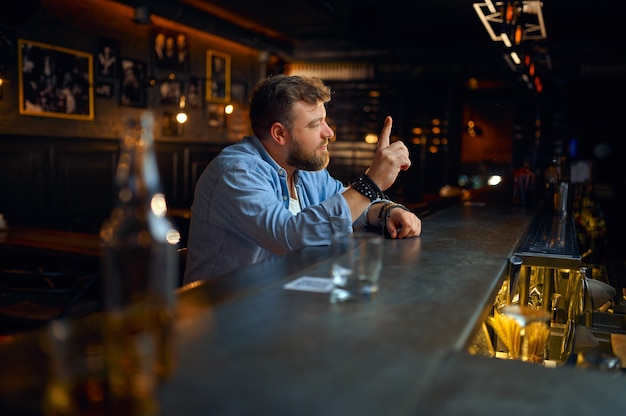 Hombre barbudo sentado en el mostrador de bar. Un hombre enojado en un pub, emociones humanas y actividades de ocio, depresión, alivio del estrés
