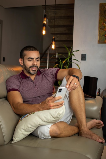 Hombre barbudo sentado en el sofá mirando el teléfono celular