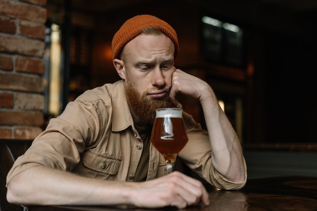 Hombre barbudo sentado solo, bebiendo cerveza en pub