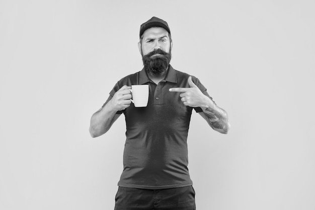 Hombre barbudo serio con gorra roja casual y camiseta señalando con el dedo la taza de café