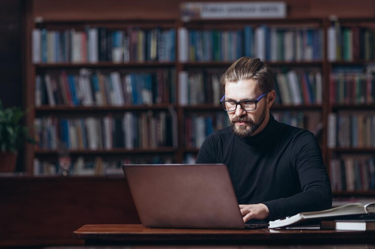 Hombre barbudo serio que trabaja en la computadora portátil en la biblioteca pública