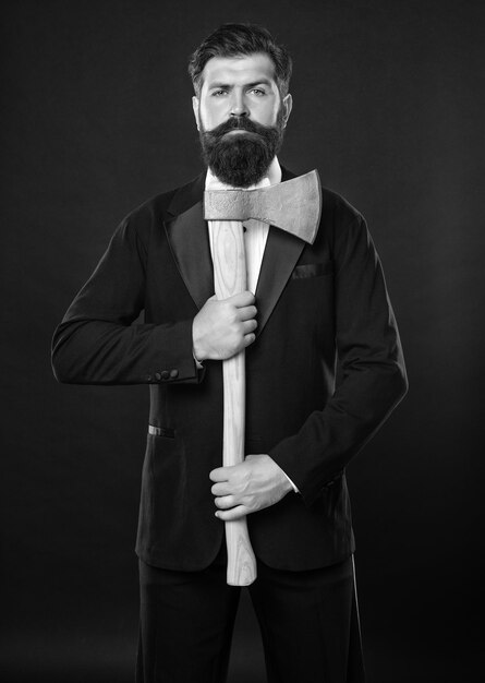 Hombre barbudo serio en traje con hacha fondo oscuro
