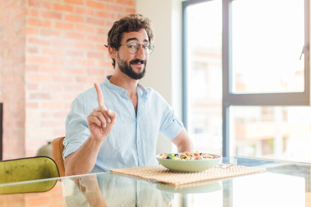 Hombre barbudo sonriendo con orgullo y confianza haciendo la pose número uno triunfalmente, sintiéndose como un líder