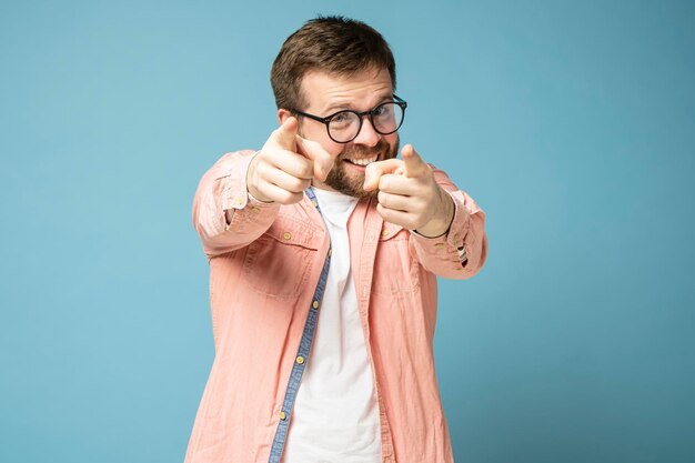 un hombre barbudo sonriente con anteojos señala insistentemente sus dedos índices a la cámara como si te eligiera a ti