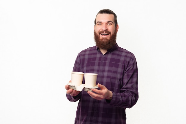 Hombre barbudo sonriente en camisa a cuadros sosteniendo dos tazas de café de papel