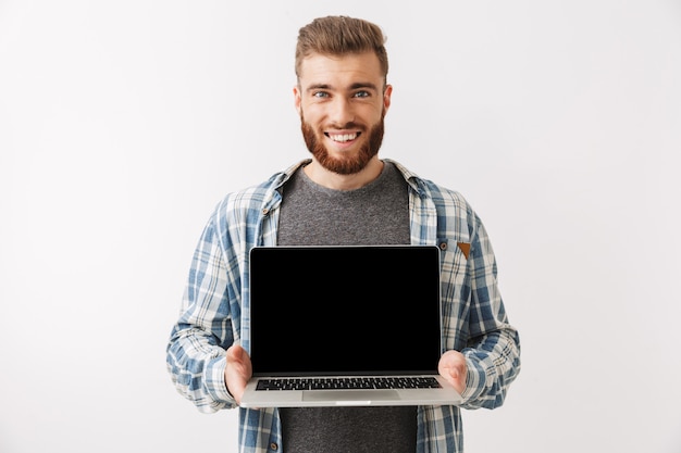 Hombre barbudo sonriente en camisa que muestra la pantalla del ordenador portátil en blanco