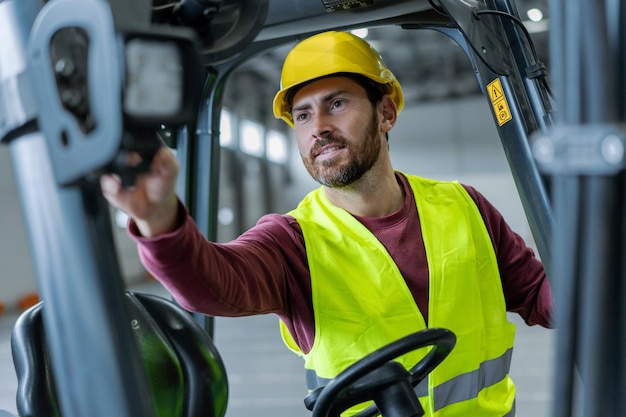 Hombre barbudo sonriente conductor trabajador profesional con casco y ropa de trabajo conduciendo carretilla elevadora