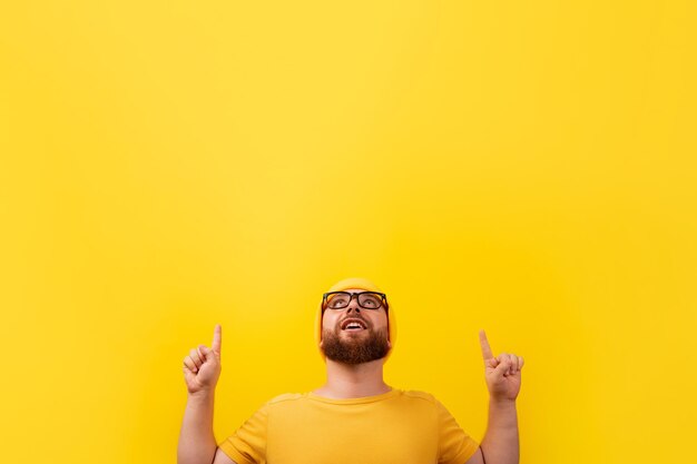 Hombre barbudo sonriente con los dedos hacia arriba, mirando hacia arriba sobre fondo amarillo, concepto publicitario