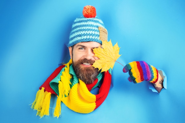 Hombre barbudo sonriente con hoja amarilla de arce otoñal en la mano hombre barbudo con sombrero colorido mirar a través