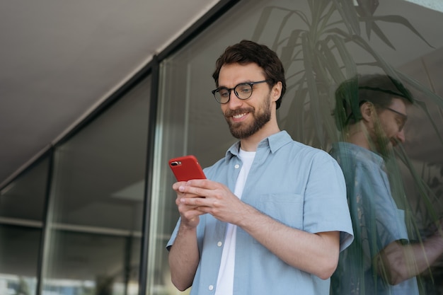 Hombre barbudo sonriente joven que usa la comunicación del teléfono móvil en línea buscando en sitio web permanente