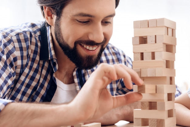 El hombre barbudo sonriente quita bloques de madera de la torre.