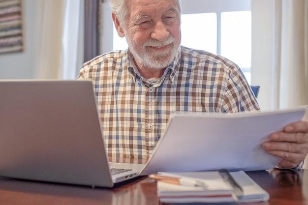 Hombre barbudo sonriente sentado en la mesa con computadora portátil y libros trabajando disfrutando de la actividad de enseñanza