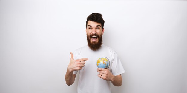 Hombre barbudo sorprendido apuntando al globo, concepto de viaje