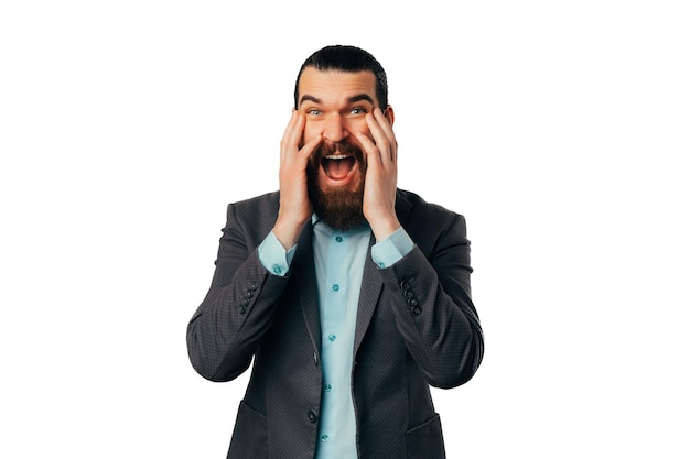 El hombre barbudo sorprendido y extasiado está mirando a la cámara y tocándose la cara