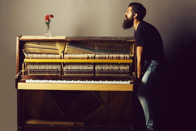 Hombre barbudo tratando de mover el piano de madera con rosa