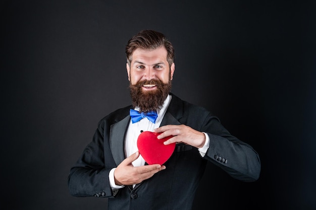 Foto hombre barbudo en tuxedo formal con pajarita comparte el corazón del amor el 14 de febrero día de san valentín amor