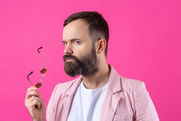 Hombre barbudo vestido con una chaqueta rosa con gafas Retrato de estudio emocional