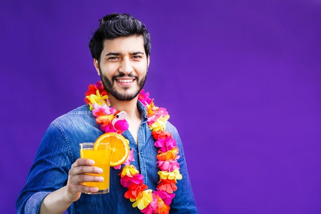 Hombre barbudo vestido con lei en el cuello sostiene una bebida de naranja sobre fondo púrpura concepto de tiempo de vacaciones tiro de estudio aislado