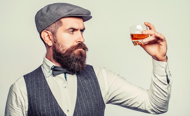 Hombre barbudo vestido con traje y bebiendo whisky brandy coñac Barbudo está sosteniendo un vaso de whisky