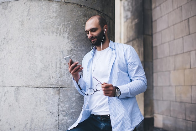 Hombre barbudo viendo teléfono inteligente con auriculares al aire libre