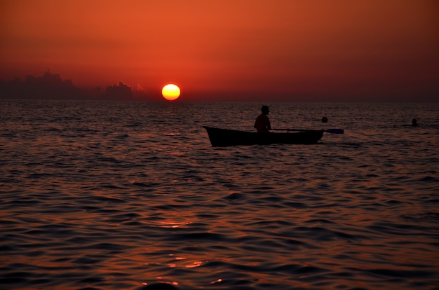 Hombre en un barco en el fondo de la puesta de sol sobre el mar