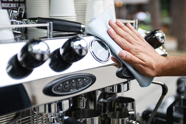 Hombre barista limpieza máquina de café espresso después de la jornada laboral