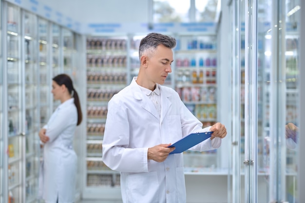 Hombre de bata blanca con carpeta en farmacia