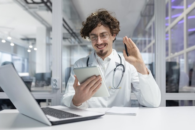 Un hombre con una bata médica blanca con un estetoscopio se sienta en un escritorio absorto en su trabajo en una computadora portátil