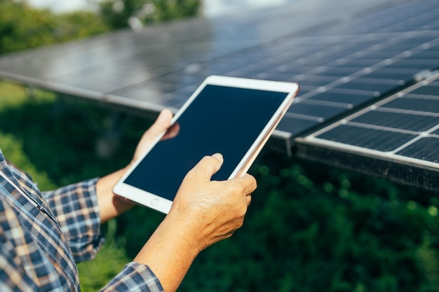 Hombre de batería solar con tableta electrónica mientras trabaja en el campo con paneles fotovoltaicos modernos