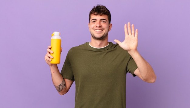 Hombre con batido sonriendo y mirando amigable, mostrando el número cinco o quinto con la mano hacia adelante, contando hacia atrás