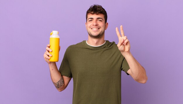 Hombre con batido sonriendo y mirando amigable, mostrando el número dos o el segundo con la mano hacia adelante, contando hacia atrás