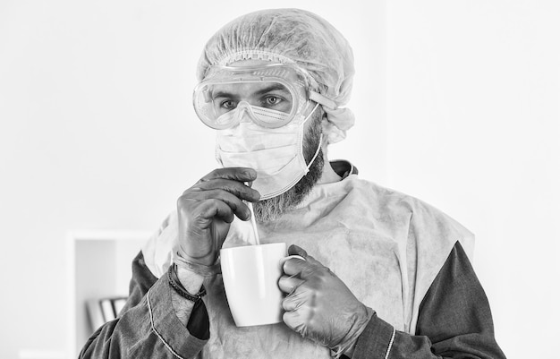 El hombre bebe café en la máscara protectora del respirador brote de pandemia de coronavirus Doctor respirando máscara respiratoria Hospital o protección contra la contaminación máscara médica de enmascaramiento facial como protección corona