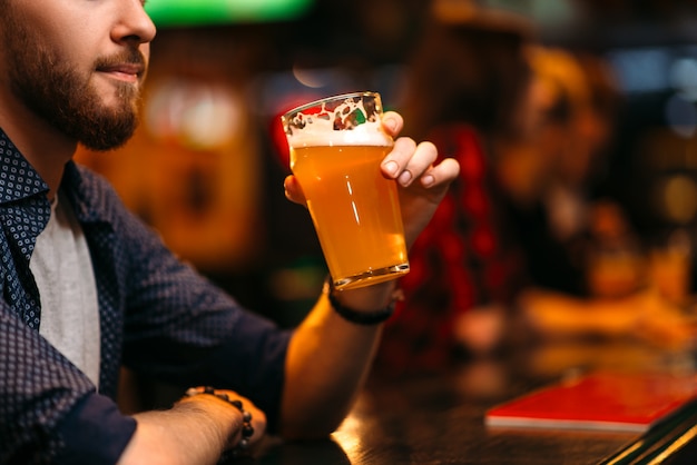 El hombre bebe cerveza en la barra del bar en un pub deportivo