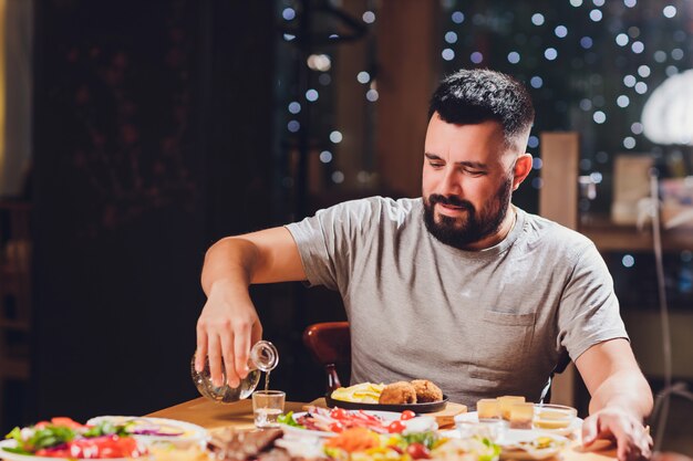 Hombre bebe vodka en una mesa grande con comida y aperitivos.