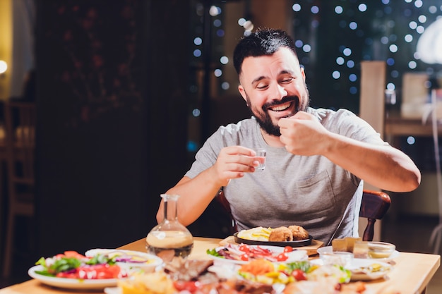 Foto hombre bebe vodka en una mesa grande con comida y bocadillos de grasa.