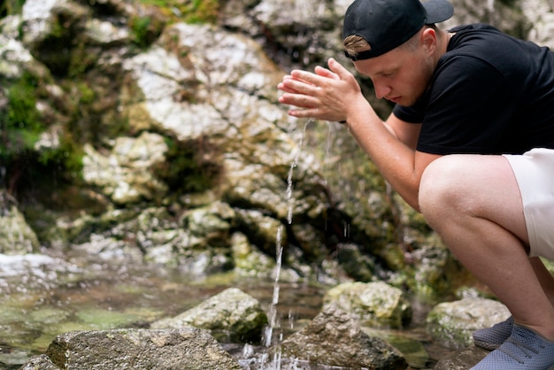 Un hombre bebiendo agua pura del río de la montaña.