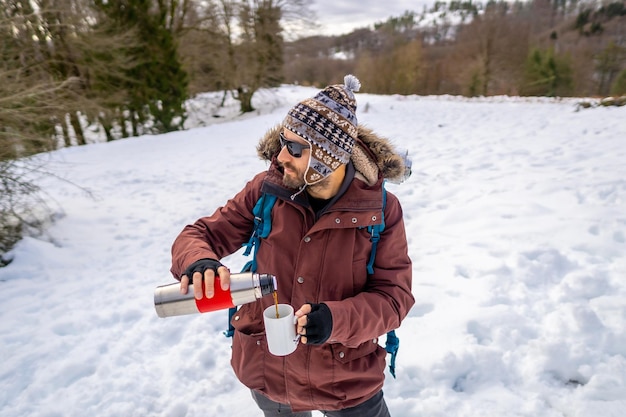 Hombre bebiendo café de un termo caliente en invierno en la nieve antes de comenzar el trekking
